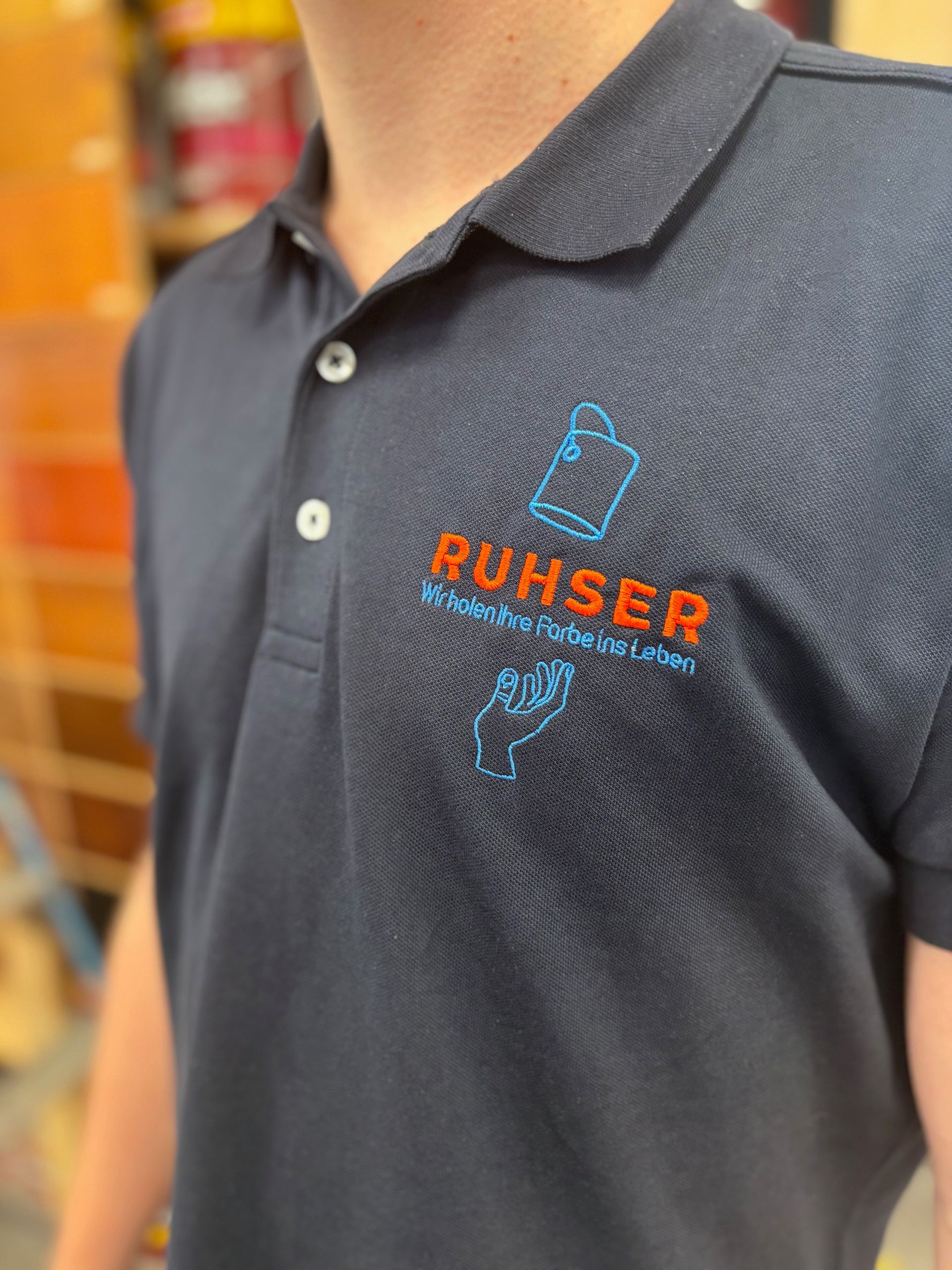Nahaufnahme eines marineblauen Poloshirts mit einem orange-blauen Logo auf der Brust.