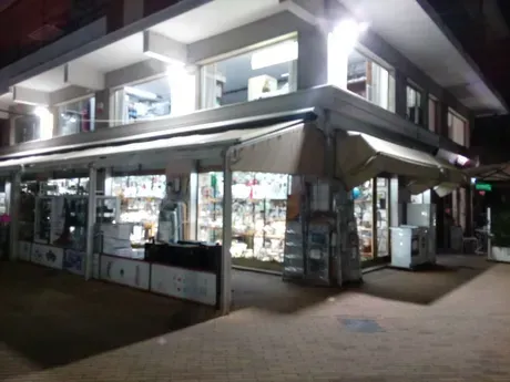 Un negozio con tante vetrine e tende da sole è illuminato di notte.