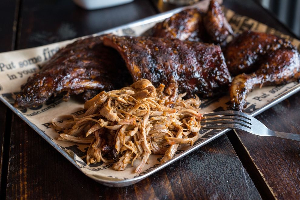 A tray of meat and noodles with a fork on a wooden table.