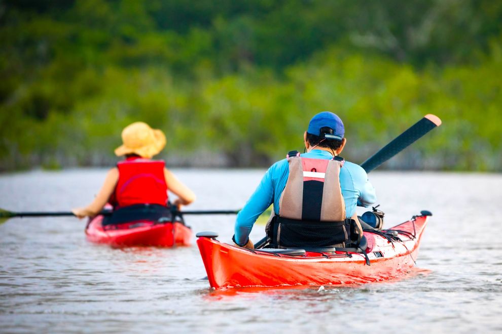 A man and a woman are paddling kayaks on a lake.