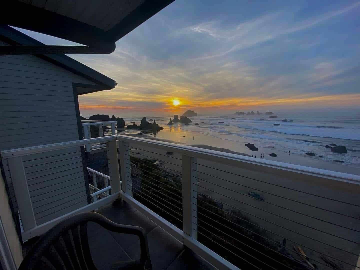 Sunset view from a balcony overlooking a beach with ocean waves and rock formations.