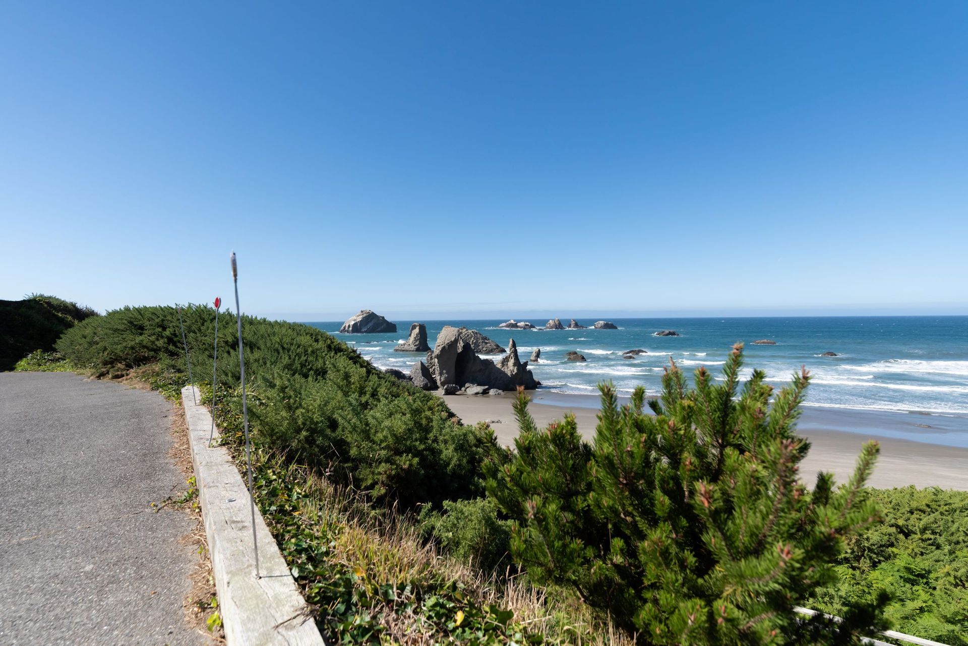 Beach and ocean view, coastal road, green bushes, blue sky, sunny day.