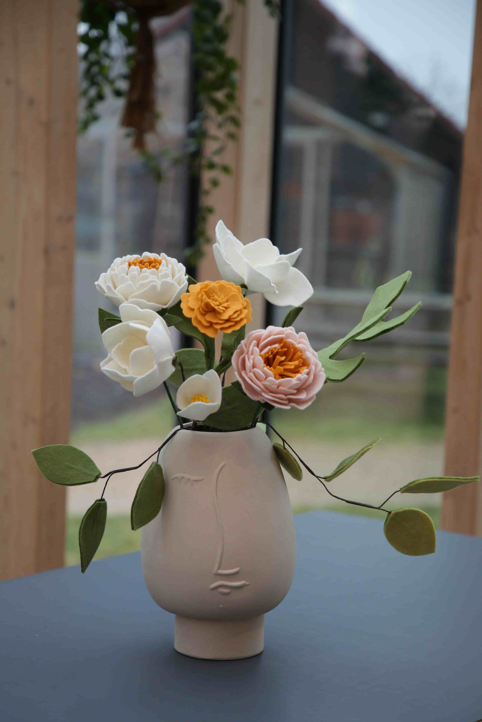 Vilten bloemen in vaas met gezicht er op
