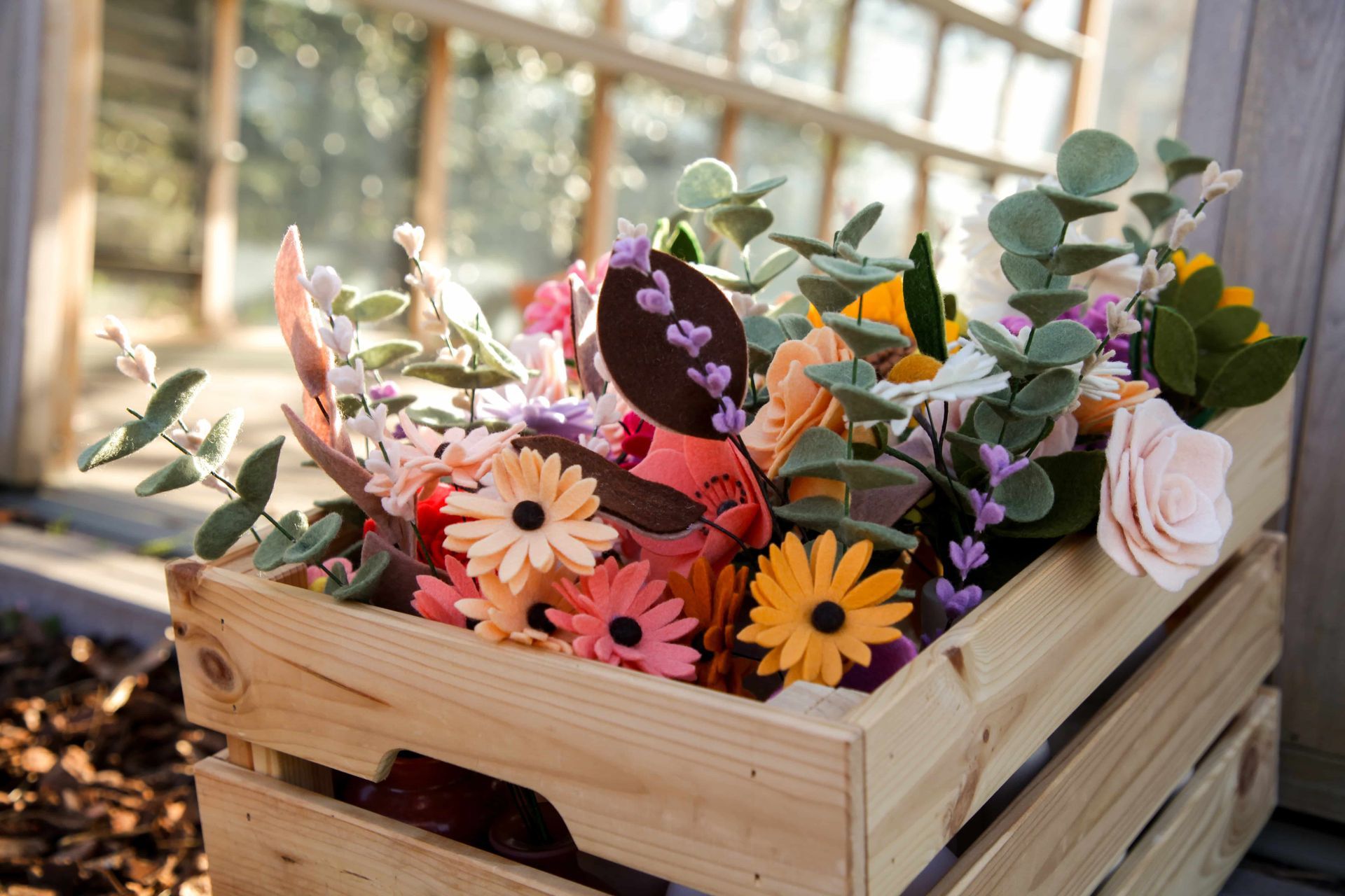 Houten krat voor een kas met kleurrijke viltbloemen

