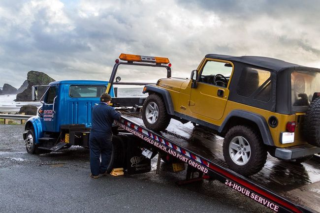 A yellow jeep is being towed by a tow truck.