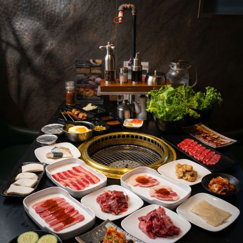 Korean barbecue spread with meat, seafood, vegetables, and dipping sauces around a grill on a dark table
