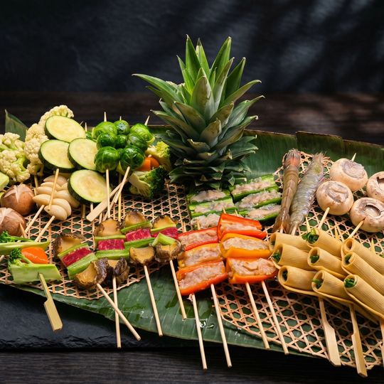 Assorted grilled skewers and vegetables arranged on a bamboo mat with a pineapple centerpiece