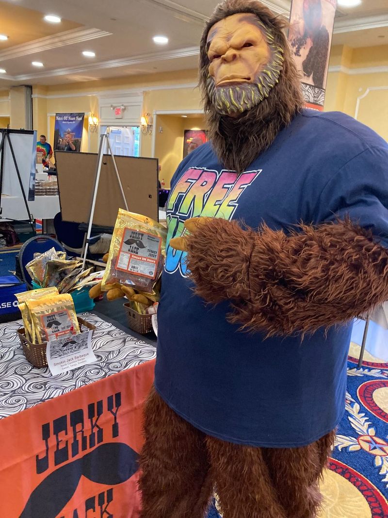 A man in a bigfoot costume is standing in front of a table that says jerky