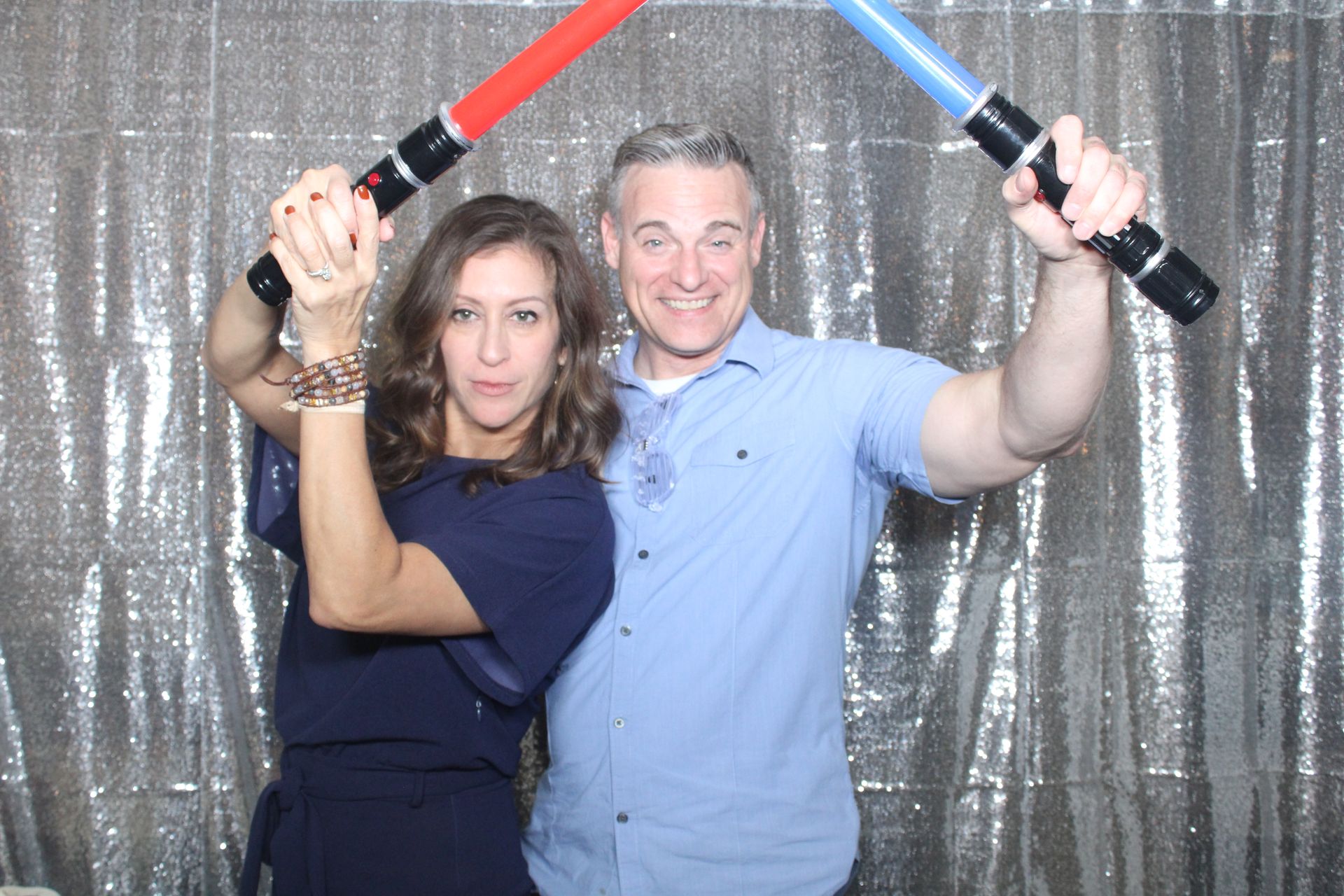 A man and a woman holding lightsabers playfully posing in the 360 Photo Booth.