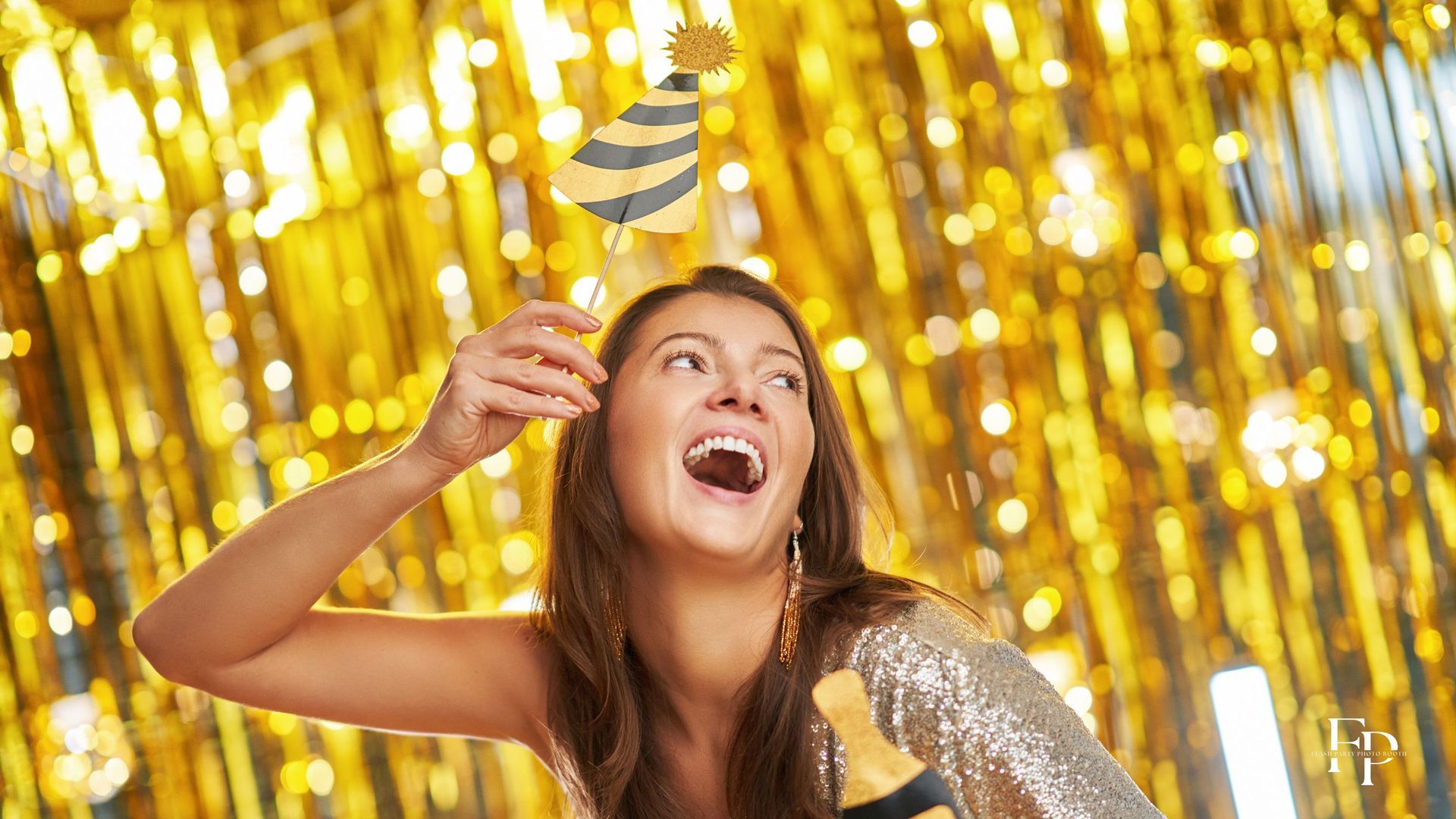 A woman holding up a photo booth prop with a golden sparkling photo booth backdrop