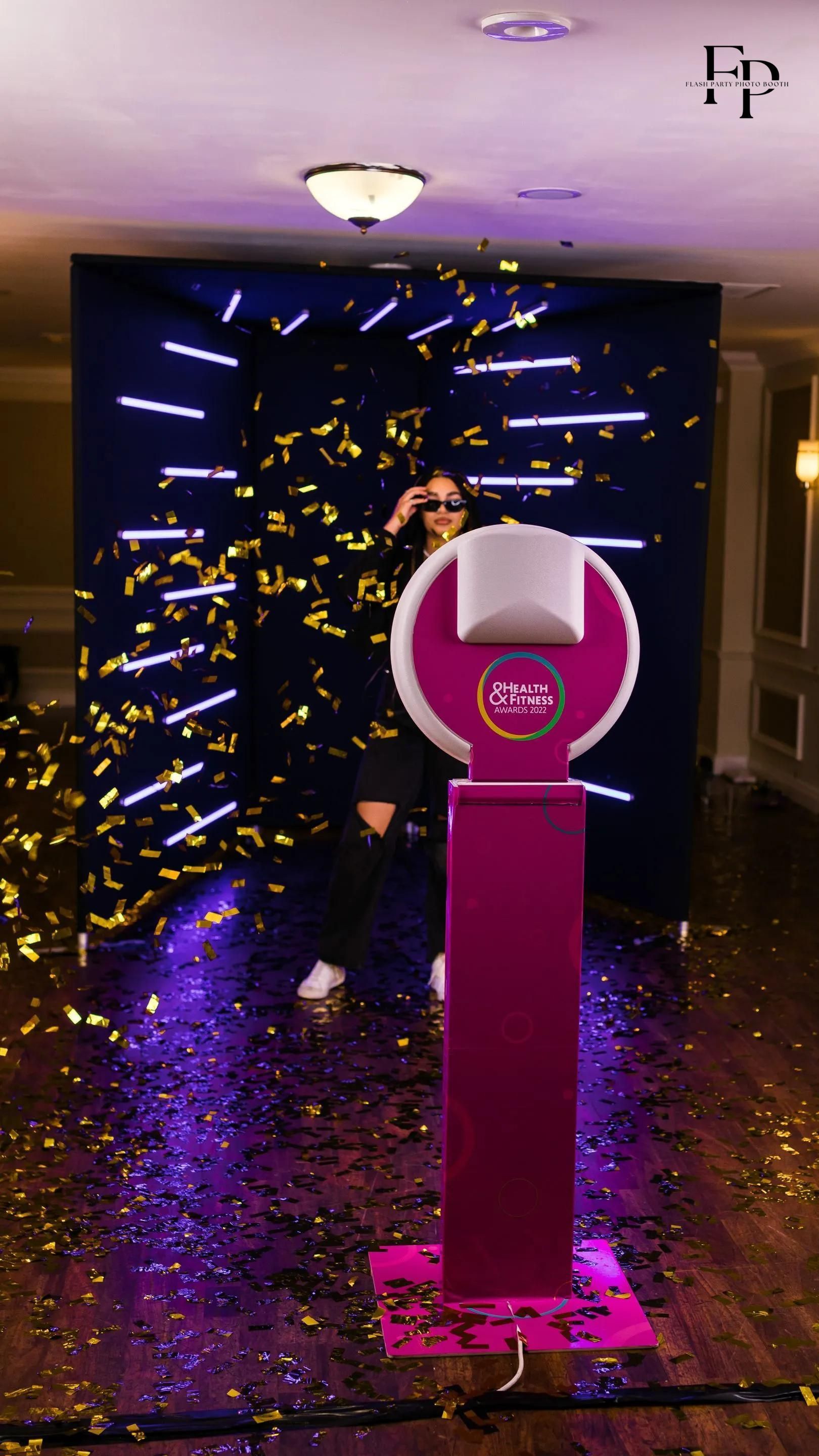 A person standing in front of a pink Selfie Photo Booth with confetti falling.