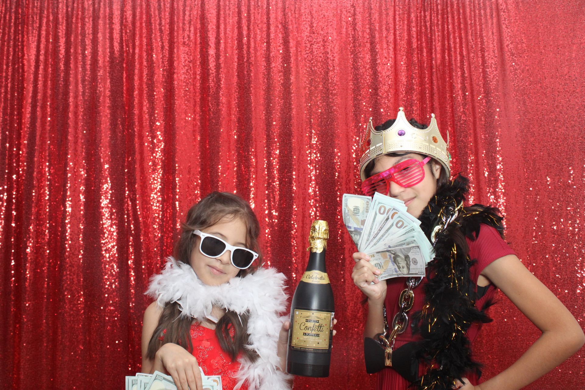 Two girls dressed in red, holding cash and a champagne bottle, posing inside the Cloee Photo Booth.