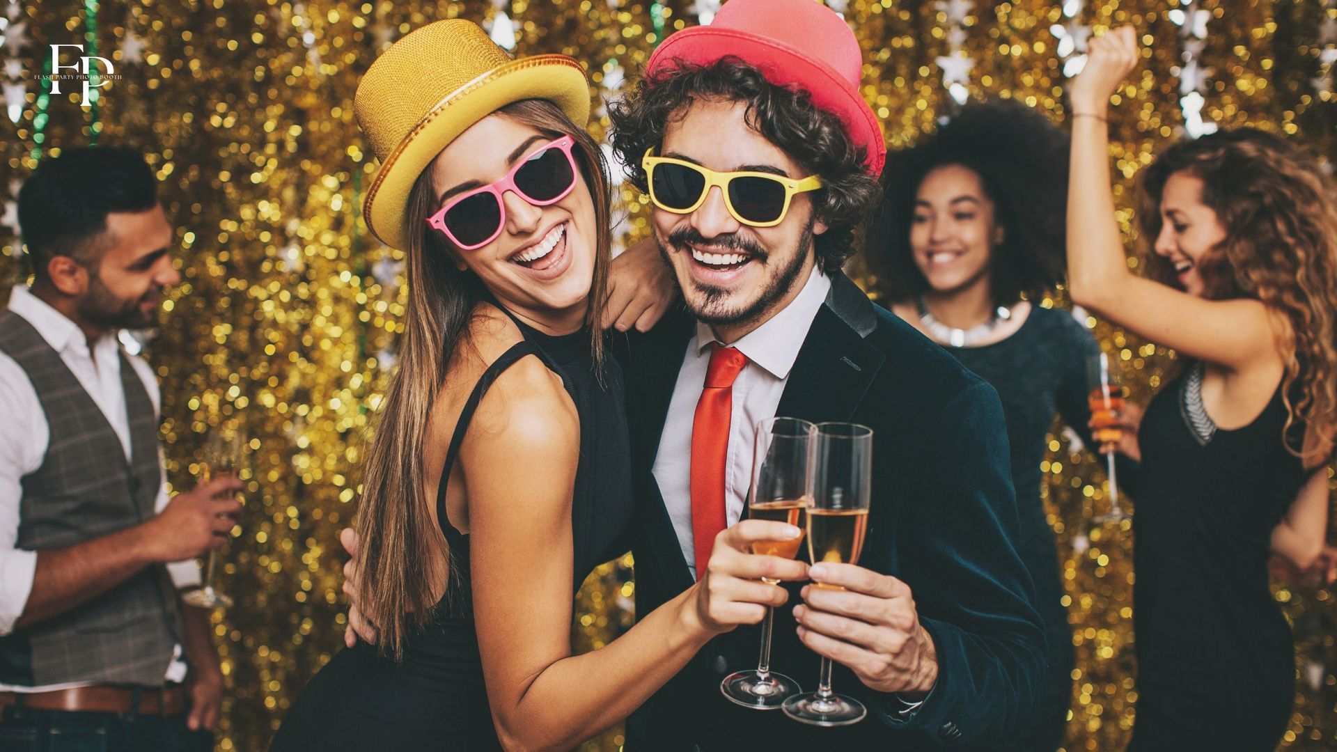 A man and woman posing at a sparkly photo booth backdrop during a graduation party in Manor holding up their drinks