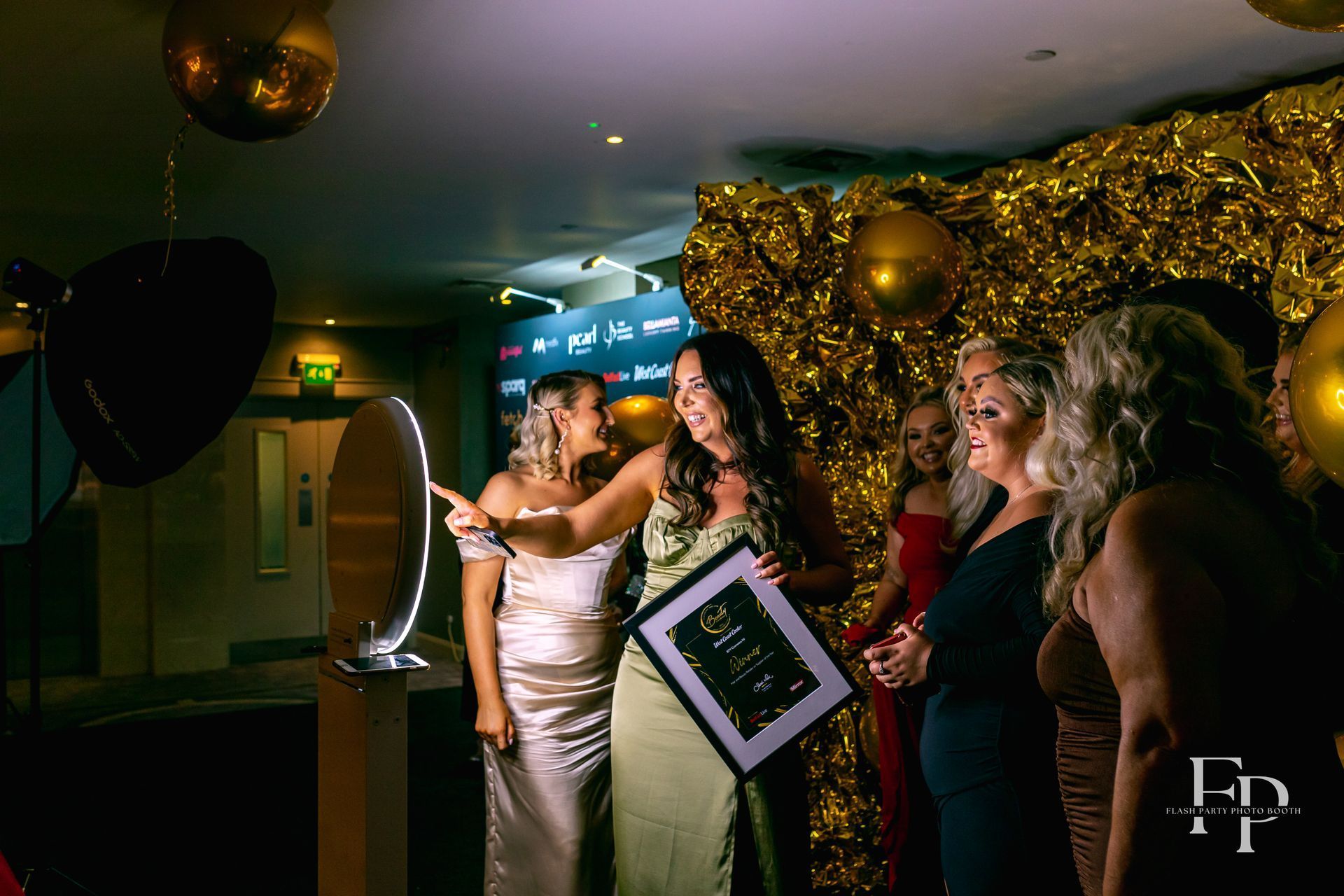 A group of women in formal dresses taking selfies in the Selfie Photo Booth.