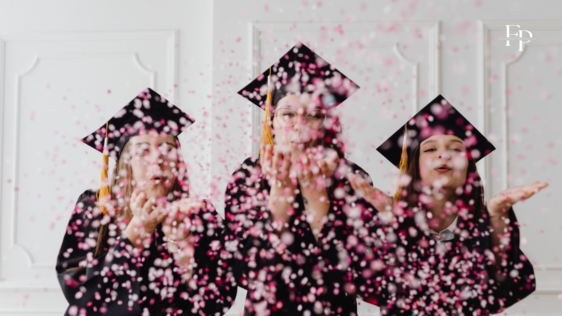 Three graduates in Charlotte blowing pink confetti