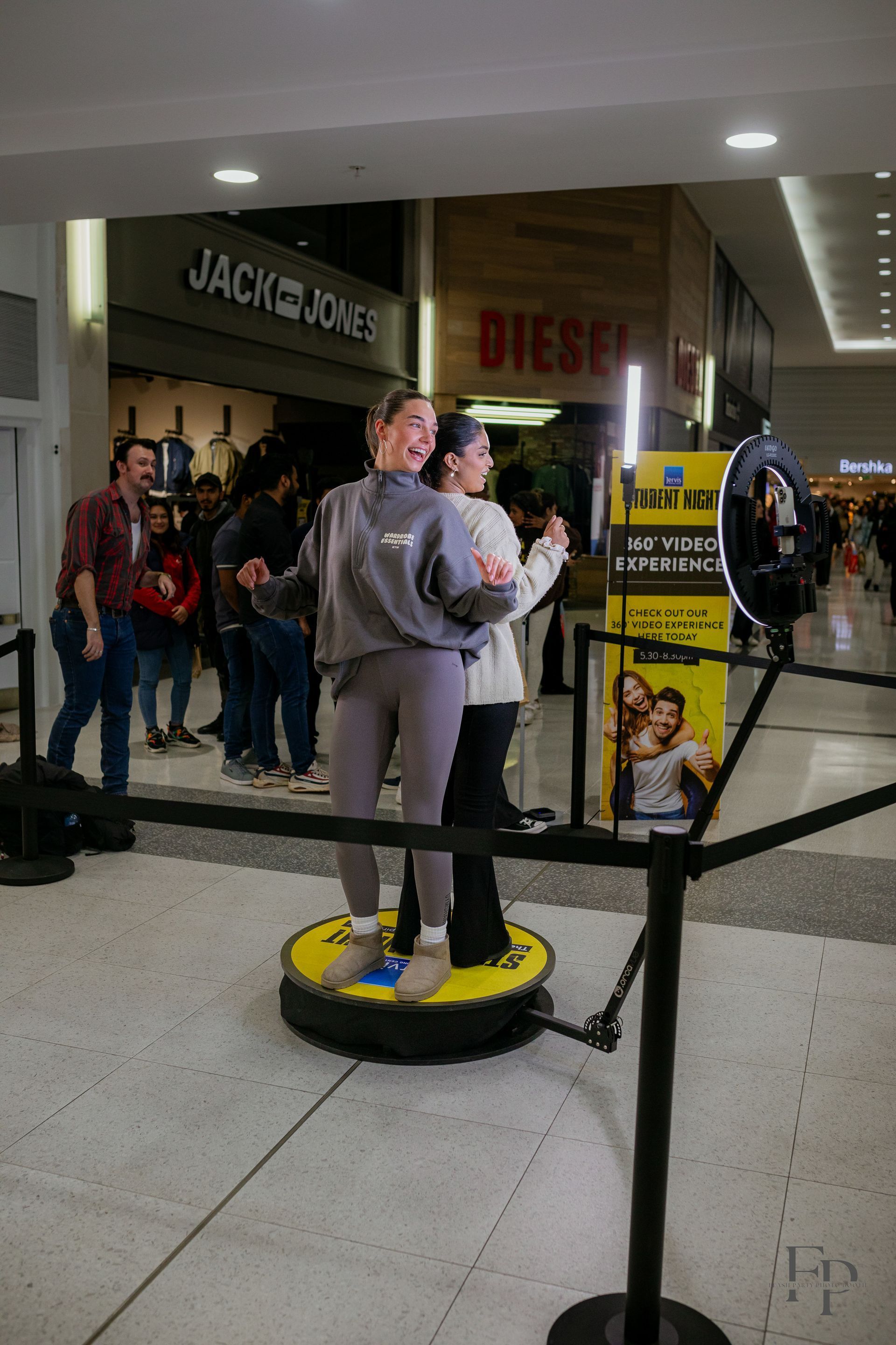 Two women standing side by side, posing for a photo in a 360 Photo Booth located in a mall.