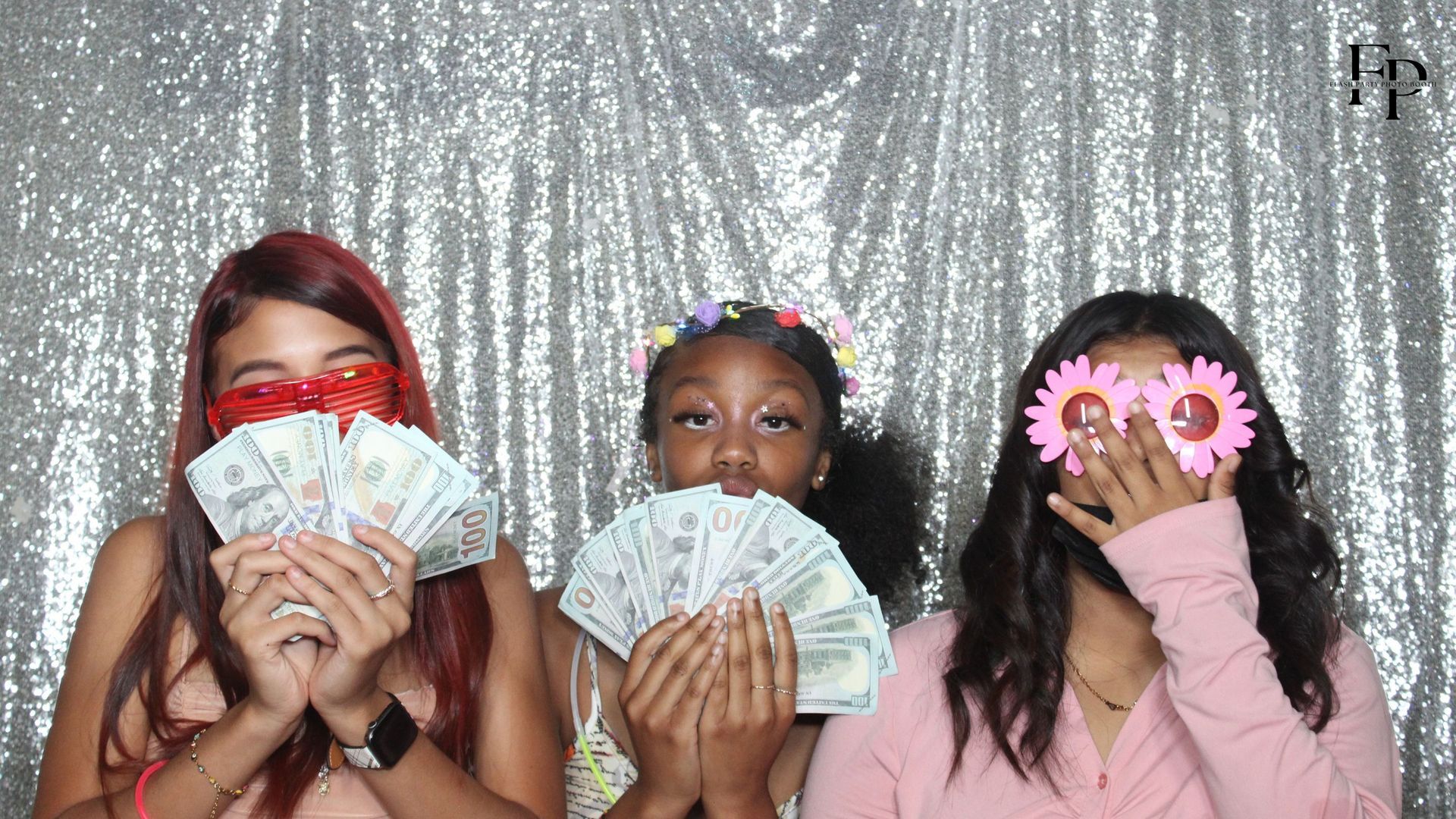 Three girls inside an Oval Mirror Photo Booth, holding money and posing for a fun picture.