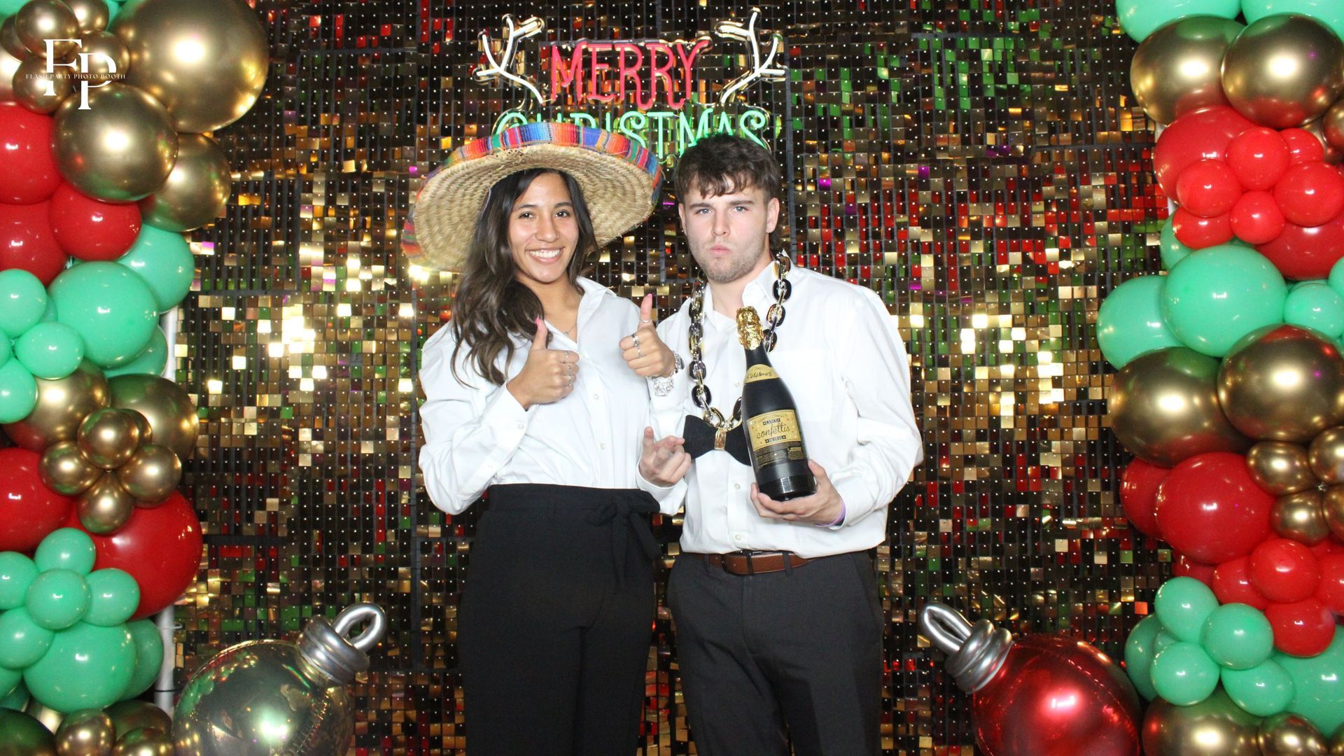 Two persons posing in the Selfie Photo Booth decorated with balloons and festive Christmas decorations.