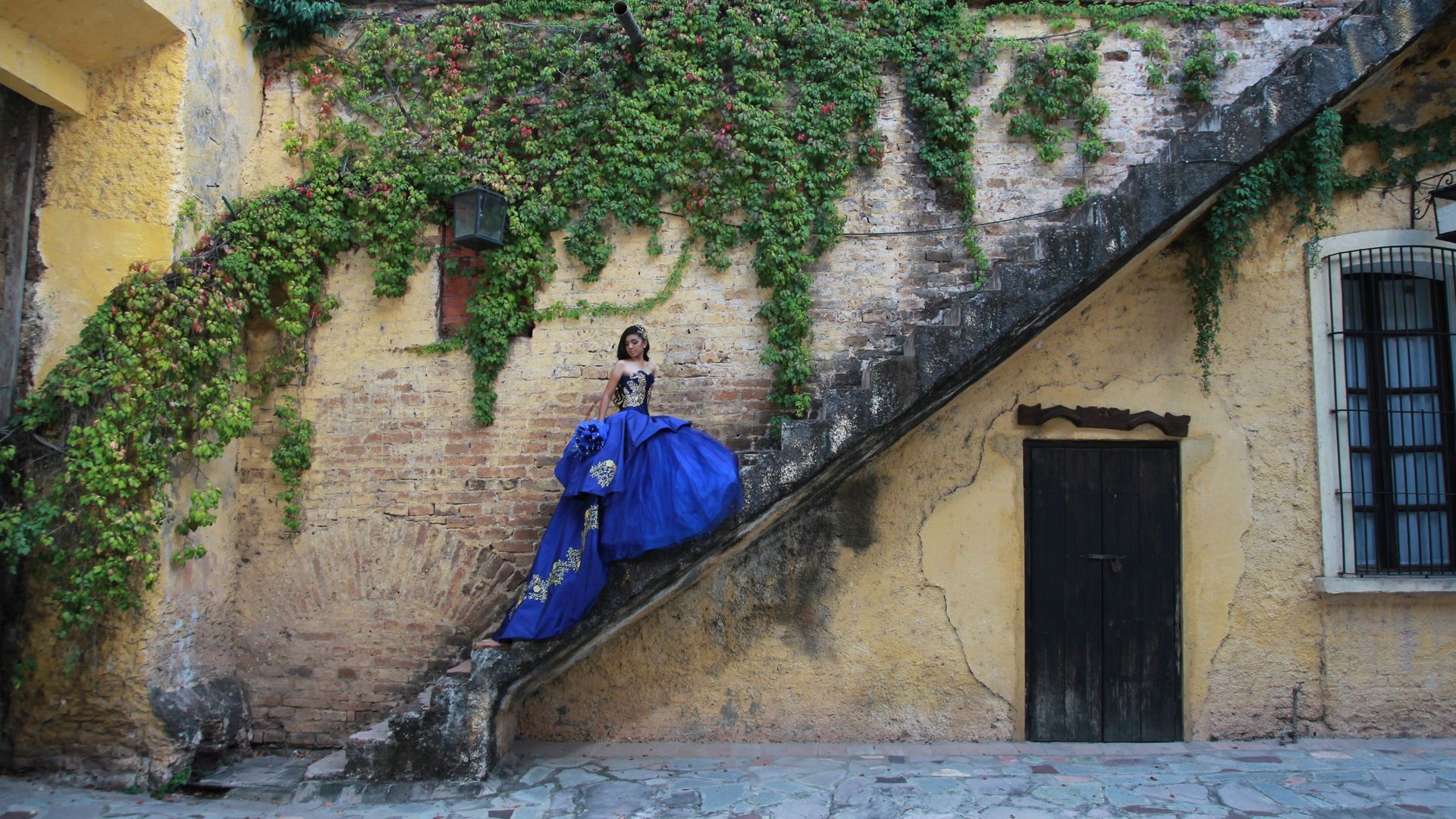 A quinceanera celebrant in a stunning blue gown going up the stairs for a photo shoot