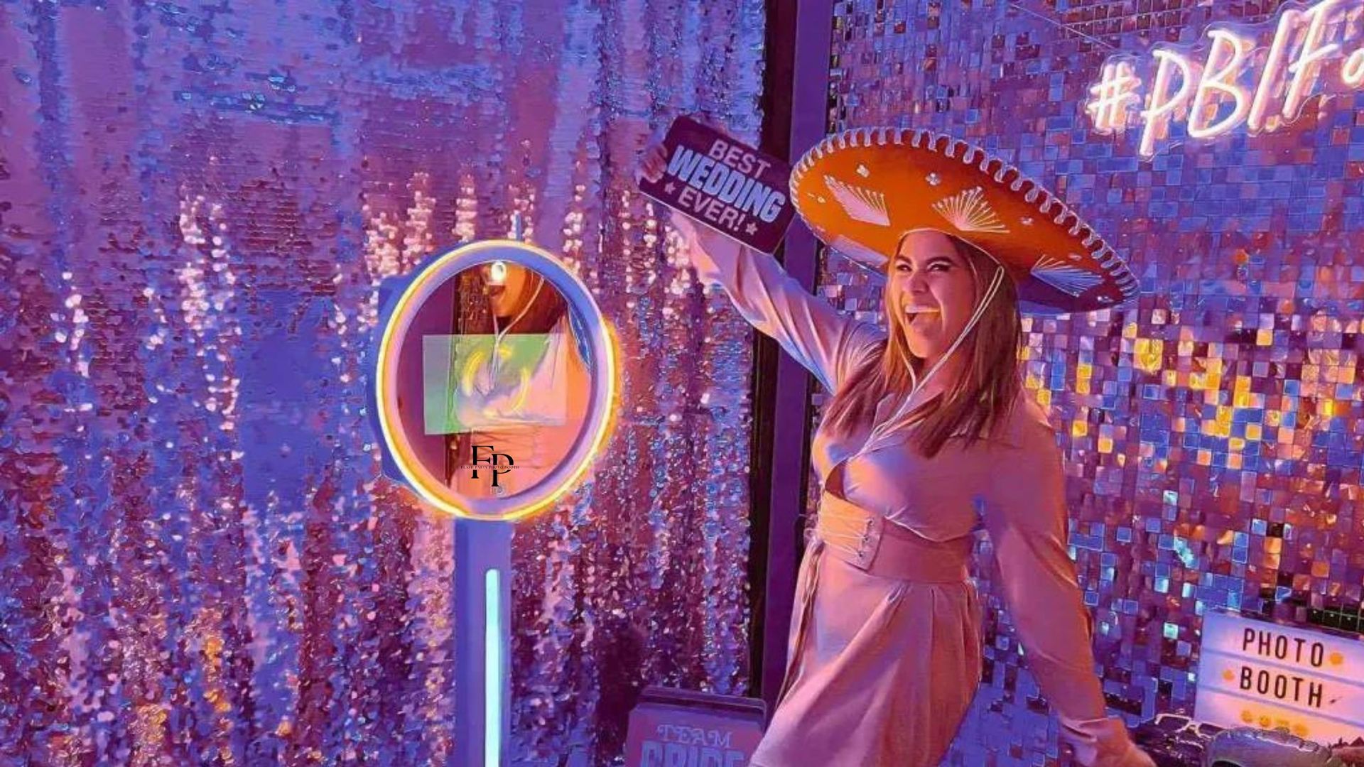 A woman wearing a sombrero and holding a sign, posing for photos in the Cloee Photo Booth.