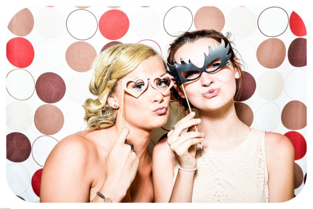 two ladies posing before a Photo Booth rental in Sugar Land with Photo Booth props