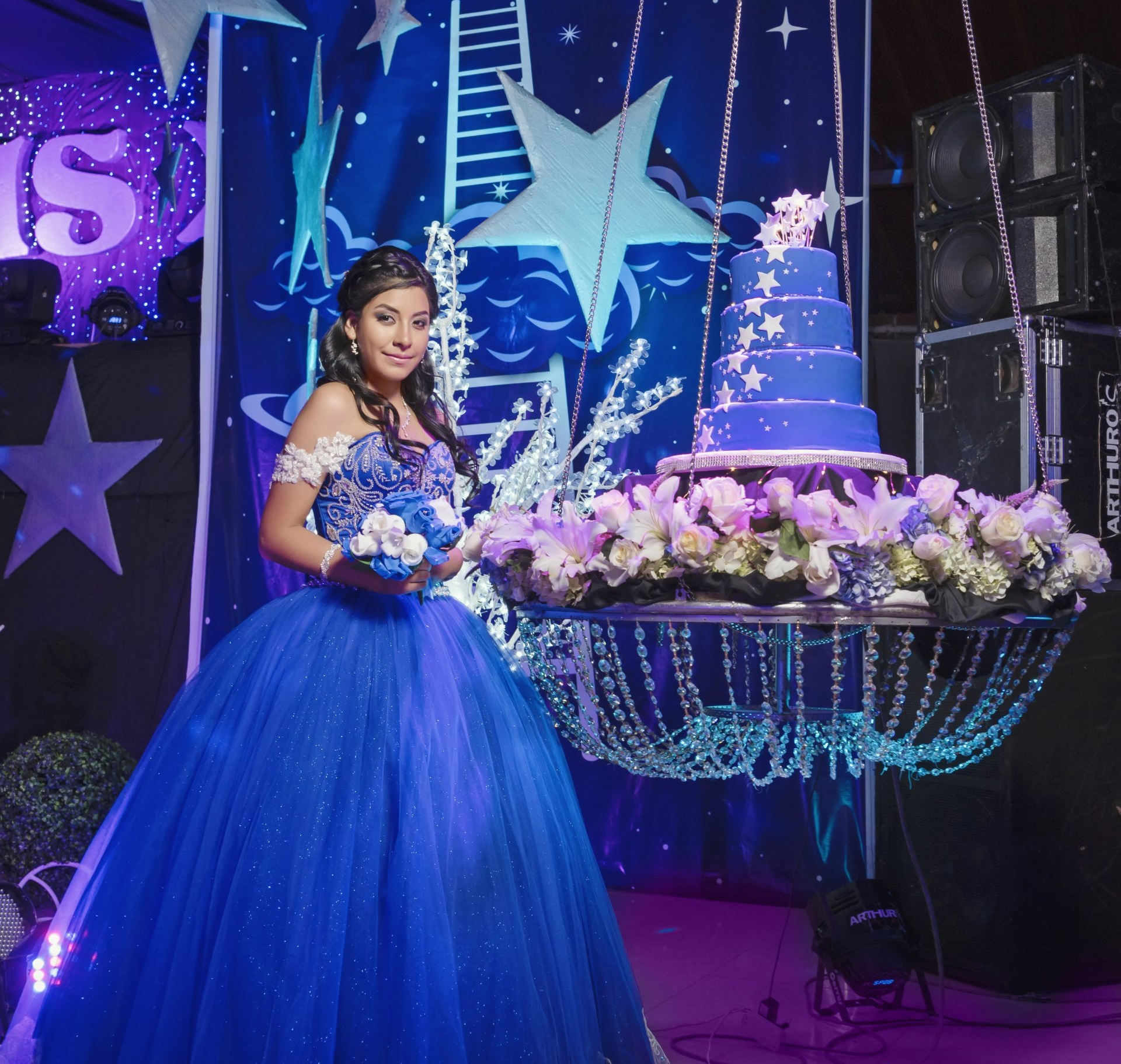 a girl wearing a blue dress standing next to a giant blue cake for her quinceanera celebration party in Austin