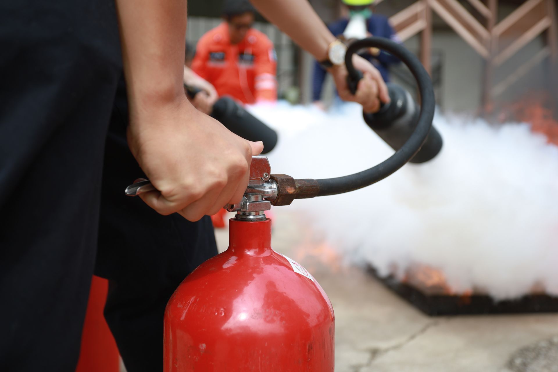 Two employees’ hands using fire extinguishers to fight a fire.
