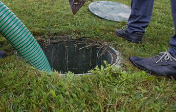 A man is pumping water into a septic tank with a green hose.