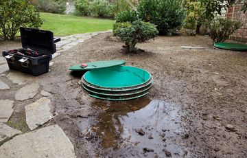 A green septic tank is sitting in the mud next to a toolbox.