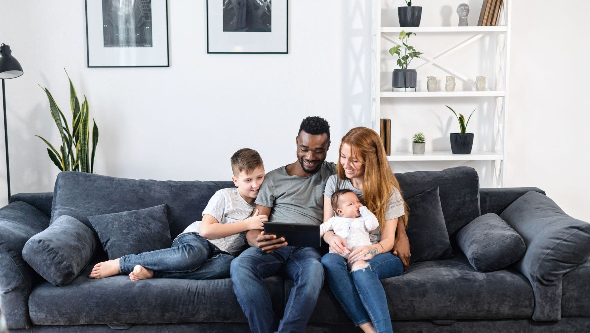 A family is sitting on a couch looking at a tablet.