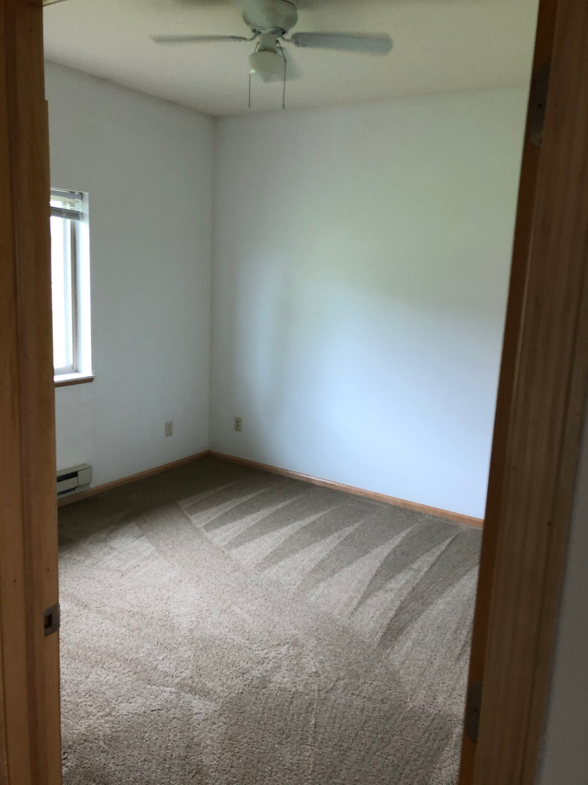 An empty bedroom with a ceiling fan and a window.