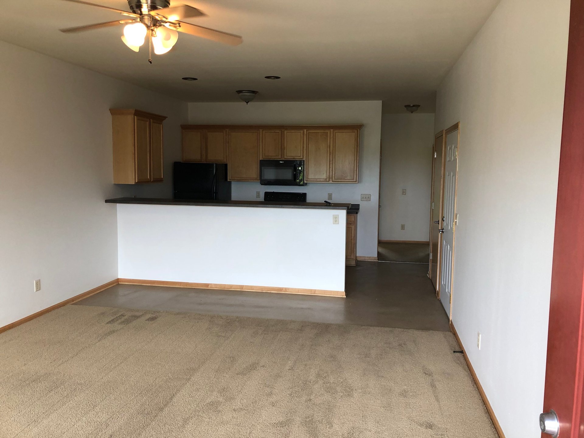 A living room with a ceiling fan and a kitchen in the background