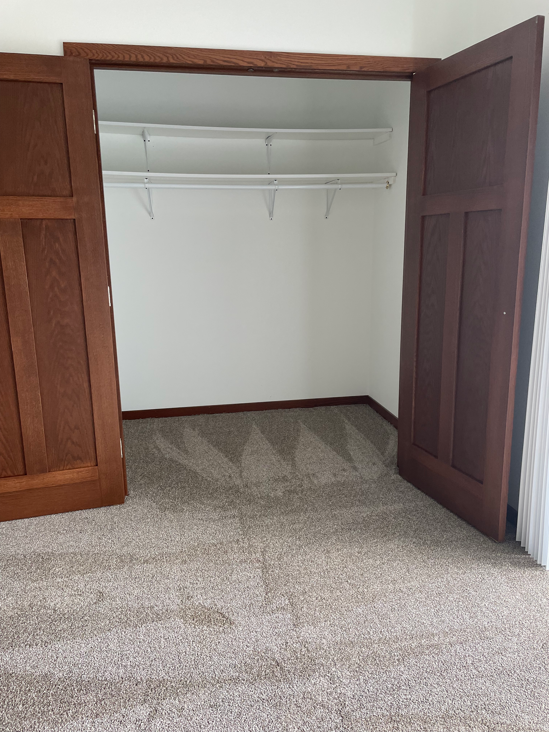 An empty closet with wooden doors and a carpeted floor