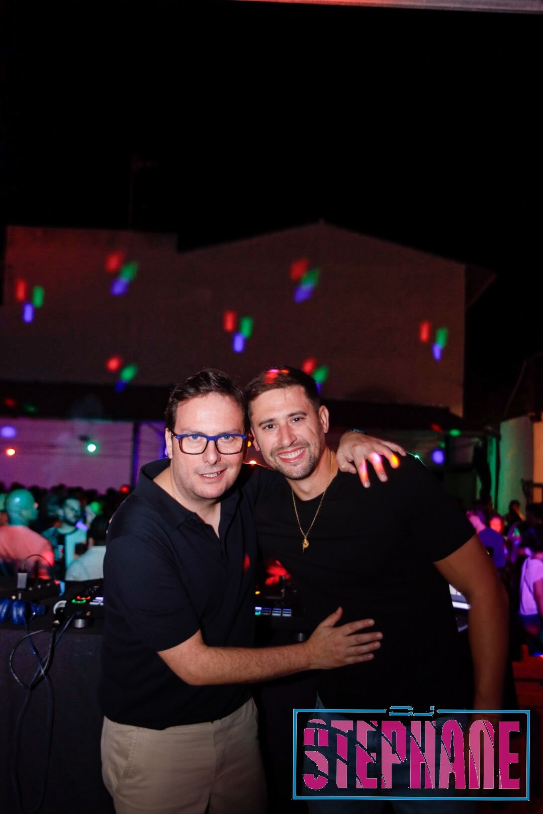 Dos hombres abrazados sonríen en un club. El logo de STEPHANE está en la esquina.