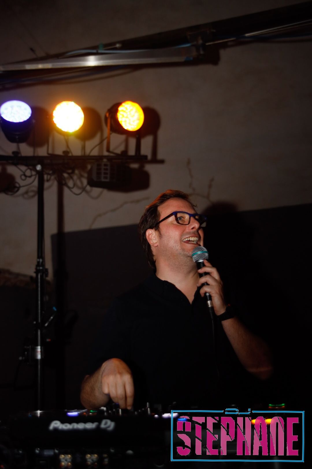 La DJ Stephanie sonriendo mientras actúa en una configuración de Pioneer DJ bajo las luces del escenario.