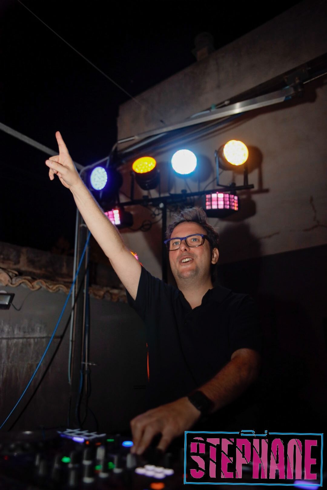 DJ Stephane con el brazo levantado, tocando música de noche, iluminado por las luces del escenario.
