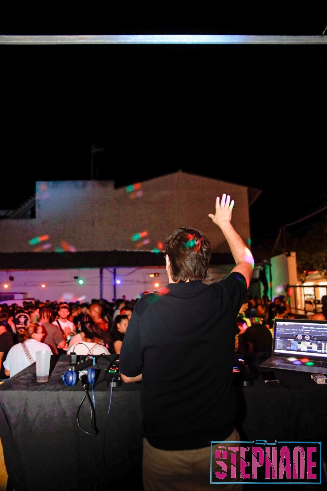 DJ en una fiesta al aire libre, levantando la mano a la multitud por la noche.
