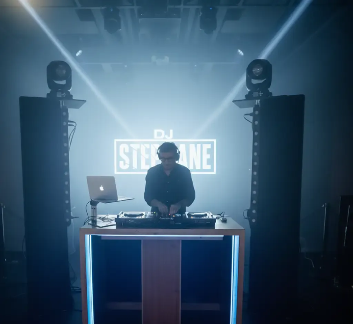 DJ en una cabina con equipo y un cartel de 