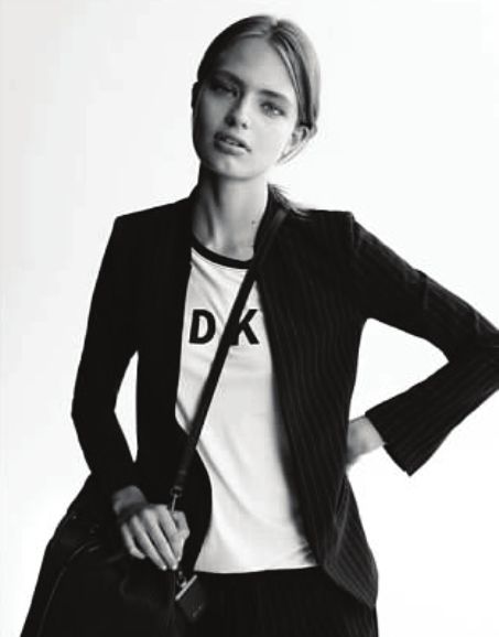 Woman wearing blazer and DKNY t-shirt, carrying a bag, posing for a photo.