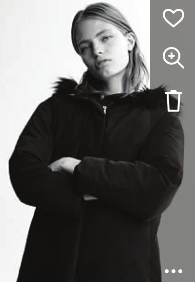 Woman in black coat with fur-lined hood, arms crossed, looking at the camera.