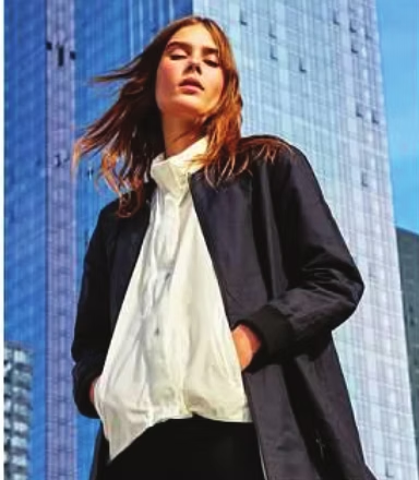 Woman in bomber jacket and white shirt in front of a tall building.