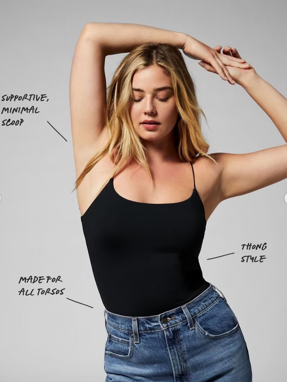 Woman in black tank top and jeans, arms raised.
