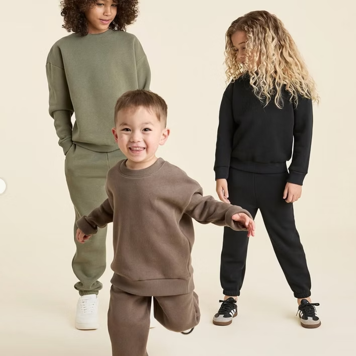 Three children in matching sweat suits pose. Olive, black, and brown outfits against a neutral backdrop.