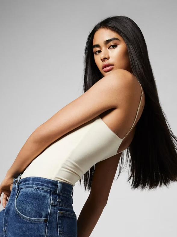 Woman in a cream-colored top and jeans, looking at the camera.