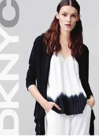 Woman in black cardigan and white top, hands in pockets, posing. DKNY logo visible.