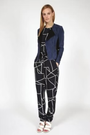 Woman in jumpsuit and blue jacket, hands in pockets, standing against a white backdrop.