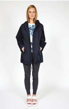 Woman in navy hooded jacket, print top, dark pants, and white sandals.