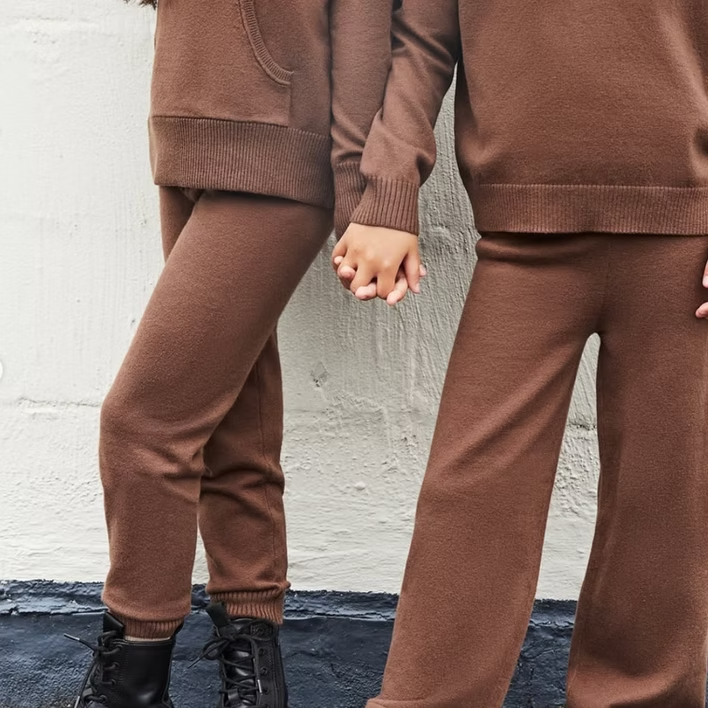 Two people in matching brown outfits holding hands against a white wall