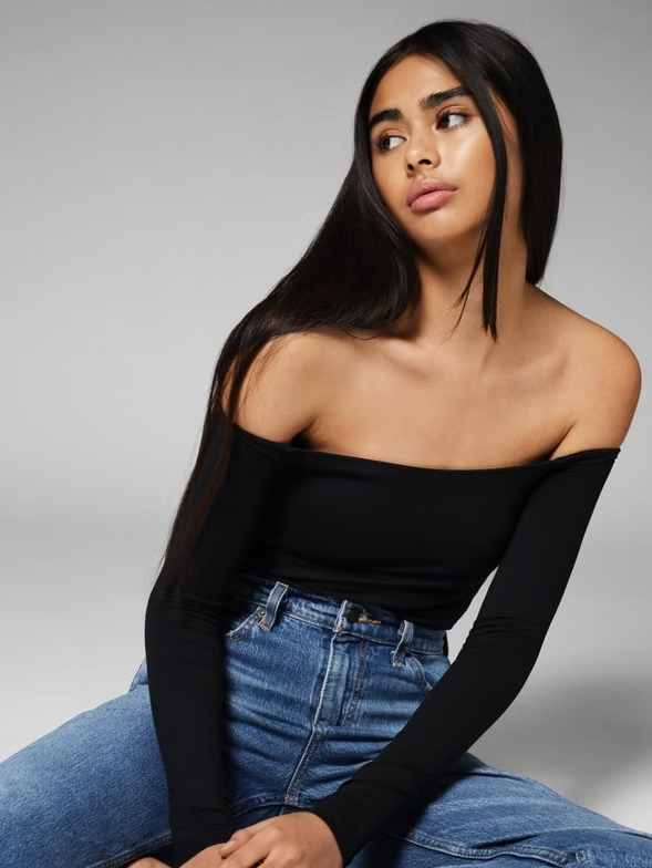 Woman in black off-the-shoulder top and jeans, sitting, looking up.