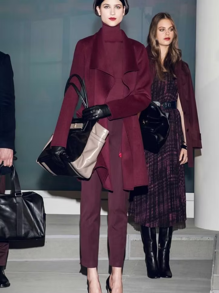 Models in burgundy outfits and bags, on steps in a fashion setting.